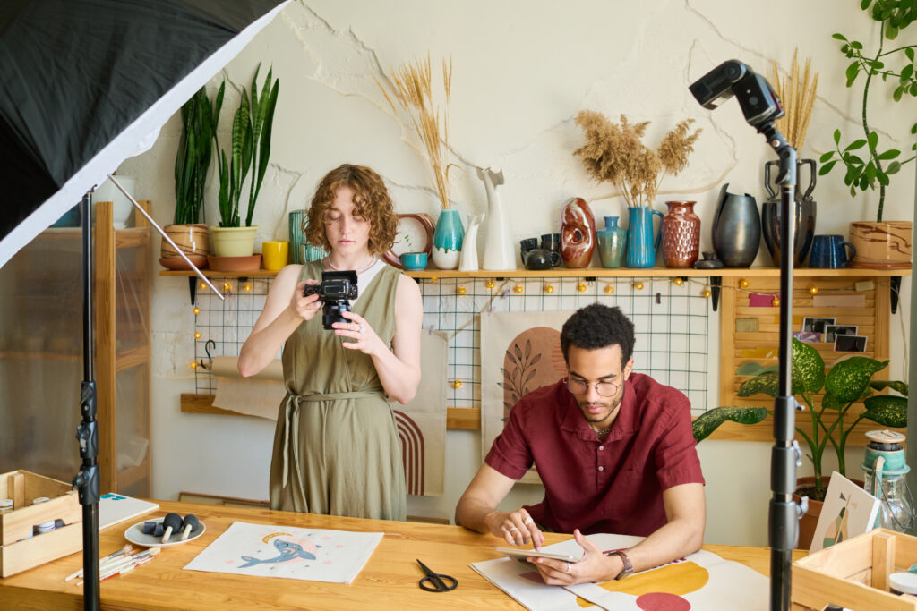 Young creative woman taking photo of drawing on table while black man networking